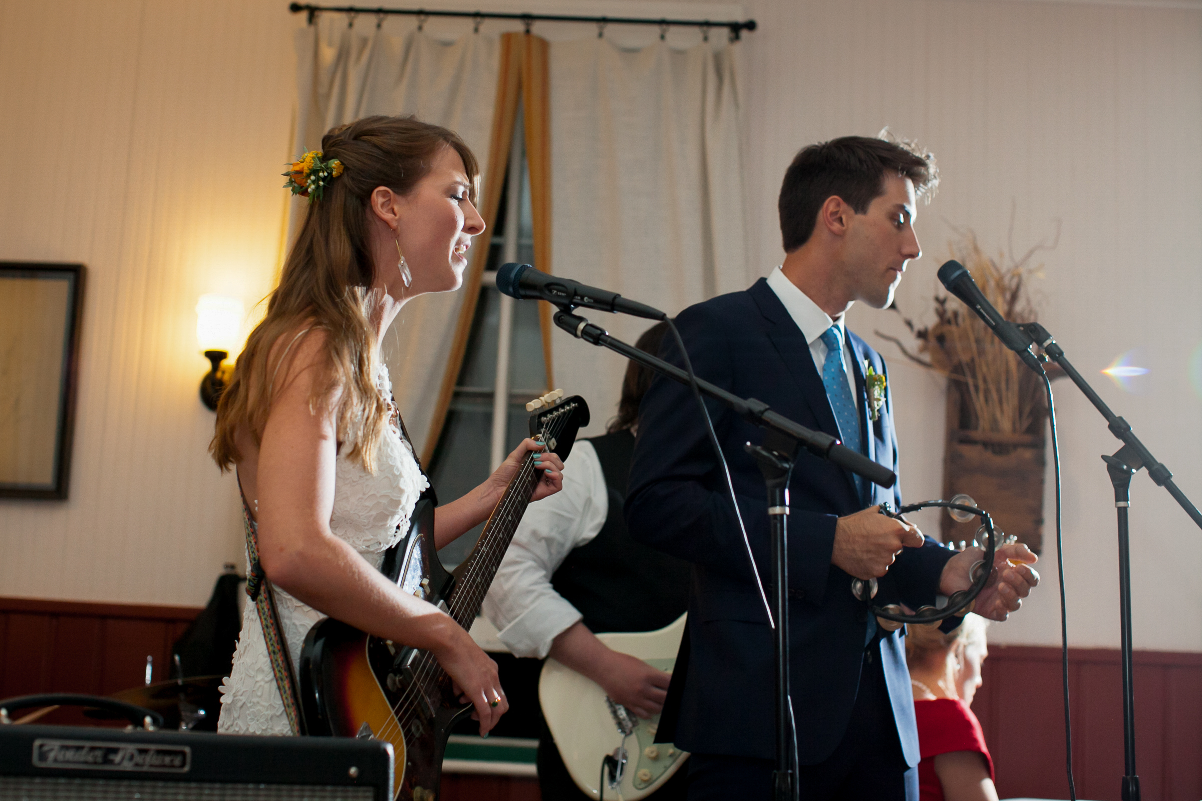 Bride playing guitar and singing with the groom playing tambourine during their Boulder Colorado wedding reception performance.