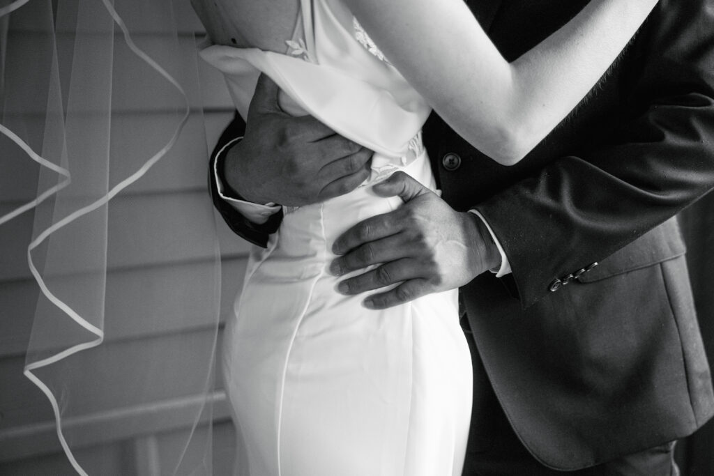 black and white photo of groom wrapping arms around bride's waist during first look
