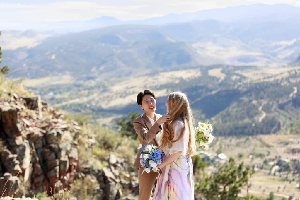 Lyons Colorado mountain wedding for an LGBTQ+ couple. Two brides share a joyful moment during their wedding on private property in Lyons, Colorado, standing on a cliffside with sweeping mountain views behind them.