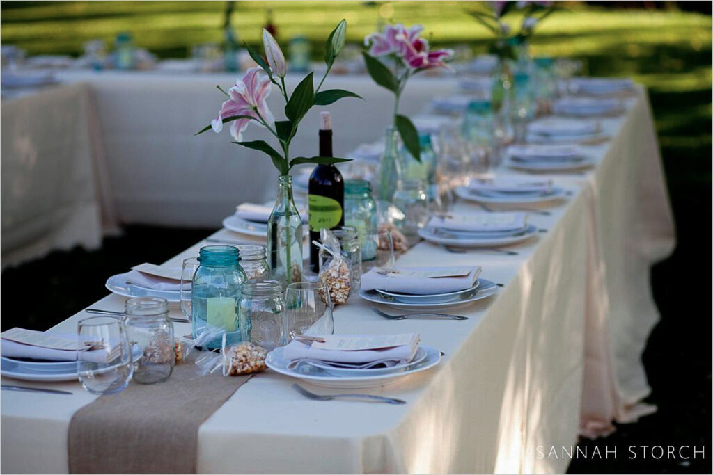 Lyons Farmette wedding reception Lyons Farmette table setting at an outdoor summer wedding in Lyons, Colorado festuring lilies, white table cloth, and brown table runner.