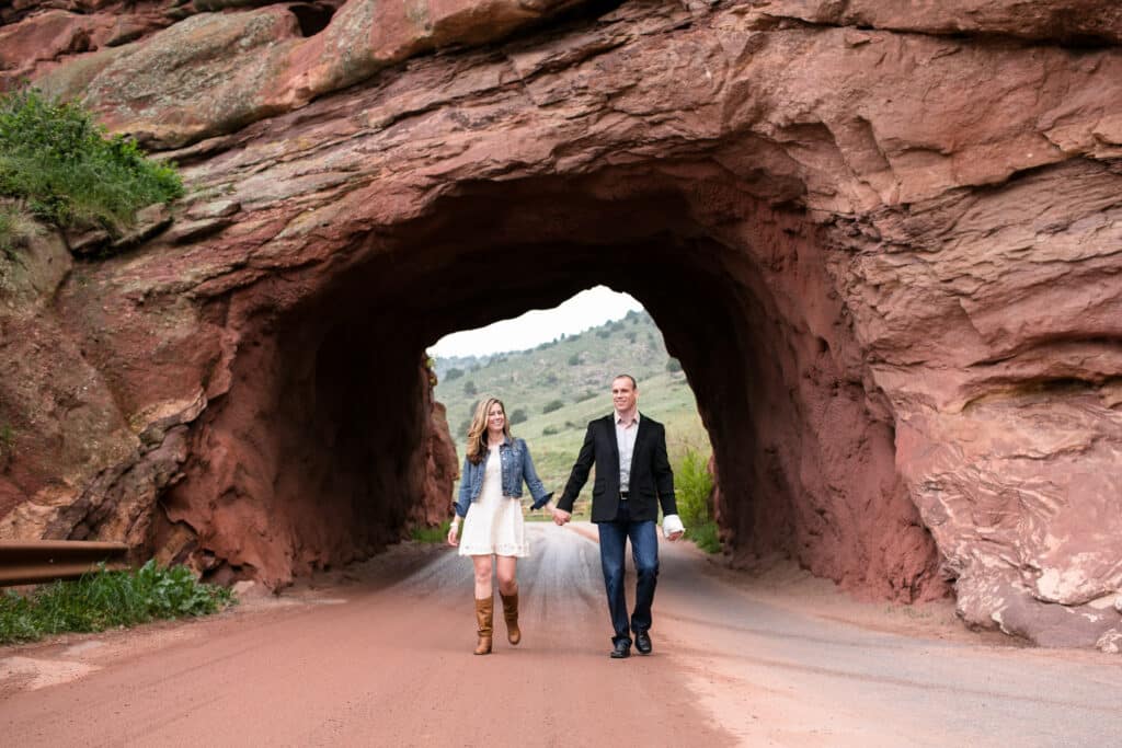 Red Rocks Colorado engagement photo. A couple holding hands and walking through a red rock tunnel during their engagement session near Red Rocks in Colorado.